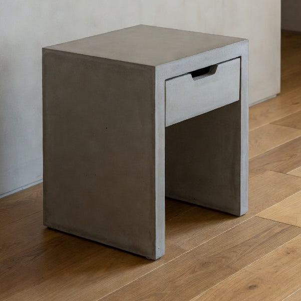 Concrete side table with a drawer against a plain wall.